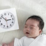 時計の傍らに眠る赤ちゃん